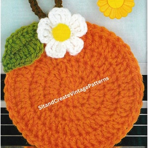 Pode incluir: Uma laranja de crochê com uma flor branca e uma folha verde. A laranja é um descanso de panela e tem o texto "SitandCreateVintagePatterns" nela.