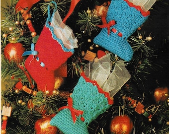 May include: Two crocheted Christmas stocking ornaments, one red and one blue, hanging on a Christmas tree with red and white ribbon bows.