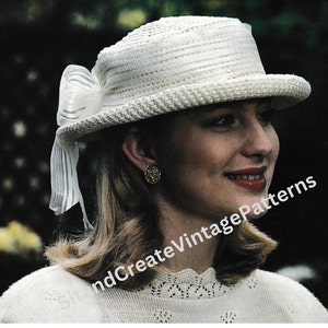 May include: A white straw hat with a large white bow on the side. The hat has a wide brim and is trimmed with a white ribbon. The woman wearing the hat is smiling and looking to the right.