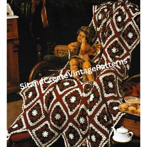 May include: A crocheted throw blanket in red, white and green, featuring a square design with snowflake motifs in the centre. The blanket is draped over a chair with a cherub figurine sitting on it.