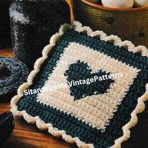 May include: A crocheted pot holder with a white center and a dark green border. The pot holder has a scalloped edge and is made with a simple stitch pattern. The text "Sit and Create Vintage Patterns" is visible in the image.
