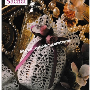May include: A white, openwork crocheted sachet bag, tied with a pink ribbon and decorated with small pink roses. The image includes the text "Sack Sachet" and "SitandCreateVintagePatterns". The bag is likely for potpourri or scented items.