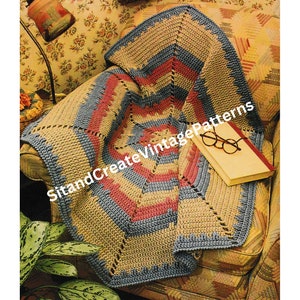 May include: A crocheted blanket in shades of blue, brown, and pink is draped over a chair. The blanket has a geometric pattern and is made with a variety of stitches. The blanket is sitting on a chair with a floral patterned fabric. The chair is in a room with a floral patterned wallpaper.