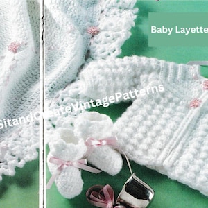 Puede incluir: Un conjunto de canastilla para bebé blanco, que incluye una manta, una chaqueta, patucos y un gorro. El conjunto está tejido a ganchillo con un punto texturizado y adornado con cintas rosas y pequeños detalles florales. Las palabras "Baby Layette Set" son visibles.