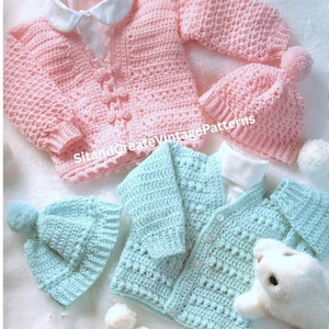 May include: Two crocheted baby sweaters and hats. One sweater is pink with white buttons and the other is light blue with white buttons. Both sets include matching hats with pom-poms.