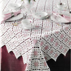 Puede incluir: Mantel de mesa de crochet blanco con un patrón floral rosa. El mantel está colocado sobre una mesa burdeos con un jarrón de flores rosas y blancas en el centro. Hay cuatro cubiertos con servilletas rosas y anillos de servilleta plateados.