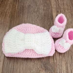 May include: A pink crocheted baby hat with a white bow and matching pink booties.