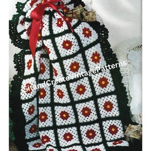 Puede incluir: Una manta de ganchillo hecha a mano con un patrón cuadrado repetitivo. Cada cuadrado presenta una flor roja con un centro amarillo sobre un fondo blanco, enmarcado por verde oscuro. La manta está atada con una cinta roja y tiene un borde verde oscuro.