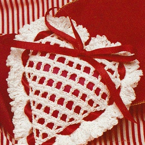 May include: A white crocheted heart-shaped pillow with a red satin ribbon tied around it. The pillow is sitting on a red and white striped fabric.