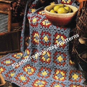 Puede incluir: Una manta de ganchillo de cuadrados de la abuela en tonos azul, rojo y amarillo. La manta está drapeada sobre una silla de madera con un cuenco de manzanas en la parte superior.