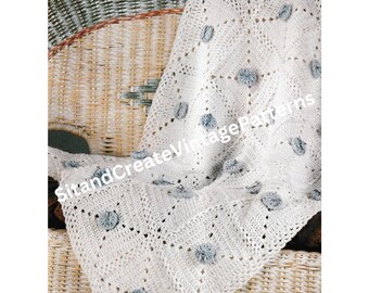 May include: A white crocheted baby blanket with gray pom-poms, draped over a wicker chair.