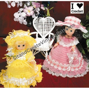Puede incluir: Dos muñecas de crochet vestidas con vestidos y sombreros de estilo vintage. La muñeca de la izquierda lleva un vestido y un sombrero amarillos, mientras que la muñeca de la derecha lleva un vestido y un sombrero rosas. Ambas muñecas sostienen accesorios, y la muñeca de la derecha está sentada en una silla blanca en forma de corazón. La imagen incluye el texto "I ♥ Crochet".