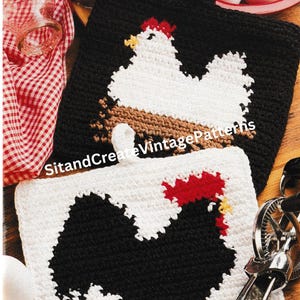 May include: Two crocheted pot holders featuring a rooster and a hen. The rooster is black and red, and the hen is white. The pot holders are made with white yarn and have a brown and black background.