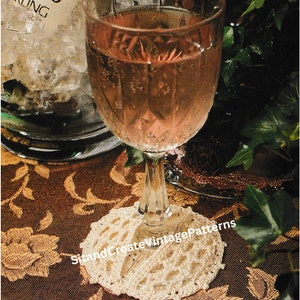 May include: A white crocheted coaster with a delicate pattern sits on a brown patterned tablecloth, with a glass of pink wine resting on top.