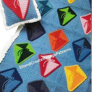 May include: A crochet baby blanket with a blue background and colorful diamond-shaped kites. The blanket has a white border and is made with a textured stitch. SitandCreateVintagePatterns is printed on the blanket.