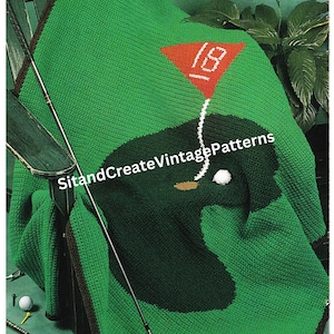 May include: Crochet golf course afghan with a green background, brown border, and a red flag with the number 18. There are golf clubs and golf balls on the green surface.