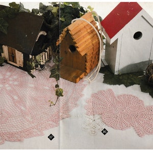 May include: A still life featuring handmade birdhouses and crochet doilies. The birdhouses are made of wood and painted in various colors. The crochet doilies are pink and white, with intricate lace patterns. A small nest with blue eggs is also present.