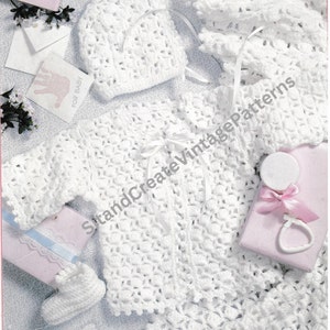 May include: White crocheted baby outfit set, including a hat, booties, and a jacket with a tie closure. The set is laid out on a white surface with a pink gift box and a white card that says "For Baby".