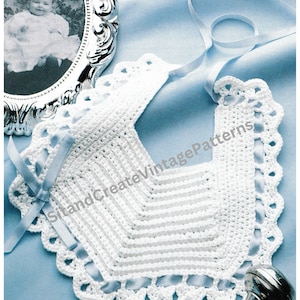 May include: A white crocheted baby bib with a scalloped edge and a blue ribbon. The bib has a chevron design and is lying on a light blue surface. A framed black and white photo is in the background.