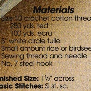 May include: Close-up of a tan paper with black text listing materials for a craft project. The text includes crochet cotton thread, white tulle, rice or birdseed, sewing thread, and a steel hook. The finished size is 1 1/2 inches across.