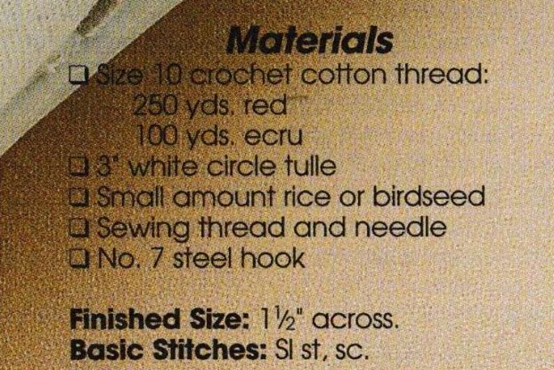 May include: Close-up of a tan paper with black text listing materials for a craft project. The text includes crochet cotton thread, white tulle, rice or birdseed, sewing thread, and a steel hook. The finished size is 1 1/2 inches across.