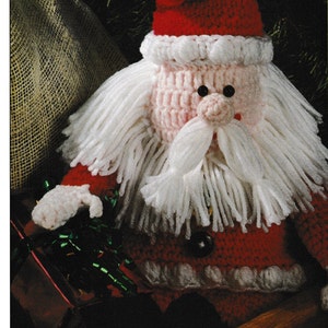 May include: Crocheted Santa Claus doll with a white beard and red hat. The doll is sitting on a wooden surface.