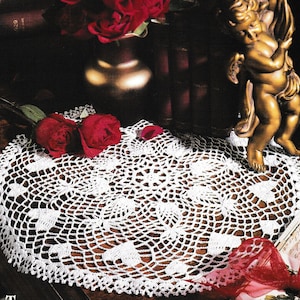 Puede incluir: Doily de crochet blanco con un delicado patrón de corazón, rodeado de rosas rojas y una figura de querubín dorada.