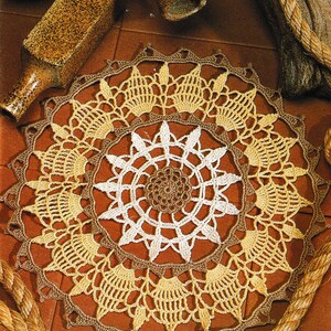 May include: A crocheted doily with a brown center and white and yellow outer rings. The doily is on a brown surface with rope.