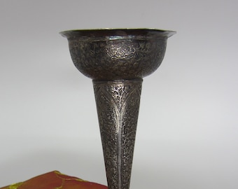 May include: A silver vase with intricate floral designs, featuring a wide, flared top and a round base. The vase is sitting on a red and gold fabric.