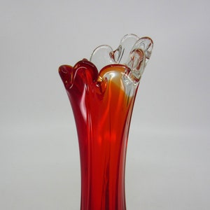 May include: A red glass vase with a clear glass rim. The vase has a wavy, organic shape and a tall, slender design.
