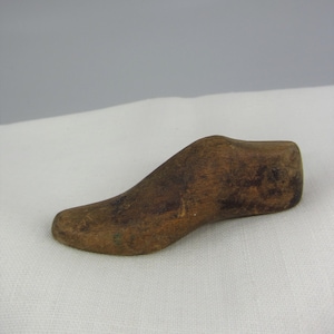 May include: A wooden shoe form, a tool used by shoemakers to shape and mold shoes. The form is brown and has a simple, rounded design.