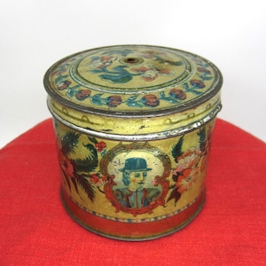 May include: A vintage tin container with a colorful floral design and a portrait of a man wearing a hat. The tin has a gold trim and a small hole in the top.
