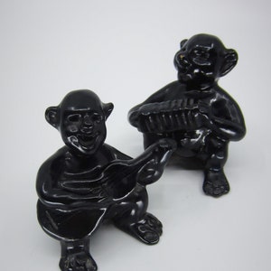 Peut inclure: Deux figurines en céramique noire de musiciens. L'une joue de la guitare et l'autre de l'accordéon.