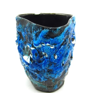 May include: A textured ceramic vase with a unique, organic design. The vase features a striking combination of deep blue, light blue, and black colors, creating a visually appealing contrast. The interior is black. This decorative piece is ideal for home decor.