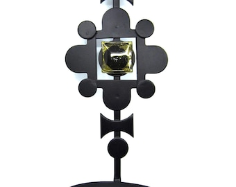 Peut inclure: Bougeoir en métal noir au design décoratif. Le support présente un dessus circulaire, un centre carré avec un insert doré et une base ronde pour accueillir une bougie. Le design est symétrique.