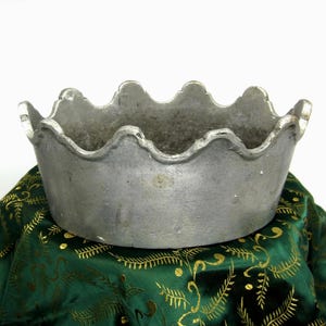 Peut inclure: Un bol en métal argenté avec un bord festonné en forme de couronne. Le bol présente une finition mate et texturée ainsi qu'une forme ovale. L'intérieur du bol semble sombre et patiné, tandis que la surface extérieure montre des nuances.