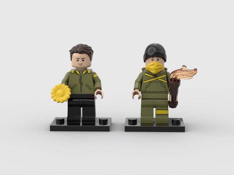 May include: Two Lego figures, one holding a yellow flower and the other a torch. Both figures wear olive green jackets, black pants, and are on black bases. One figure has a black helmet and yellow face covering.