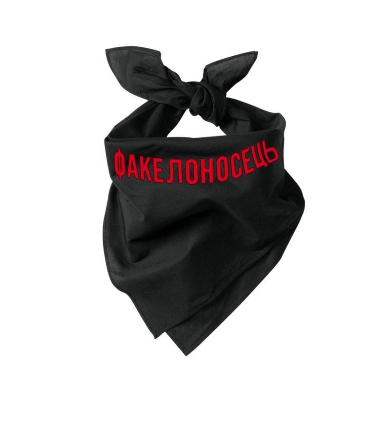 May include: Black bandana with red embroidered text. The bandana is tied at the top. The text is in a bold, sans-serif font. The ends of the bandana hang down.