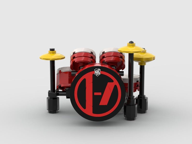 May include: A miniature drum set made of red, black, and yellow blocks. The bass drum features a black face with a red logo. Two cymbals are positioned above the drums. The set is on a white background.
