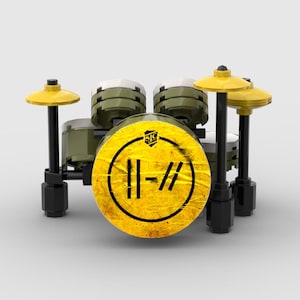 May include: A miniature drum set constructed from building blocks. The set features a yellow bass drum with a black and yellow logo, olive green drums, and yellow cymbals. The drum set is set against a plain white background.
