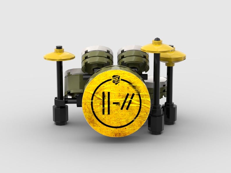 May include: A miniature drum set constructed from building blocks. The set features a yellow bass drum with a black and yellow logo, olive green drums, and yellow cymbals. The drum set is set against a plain white background.