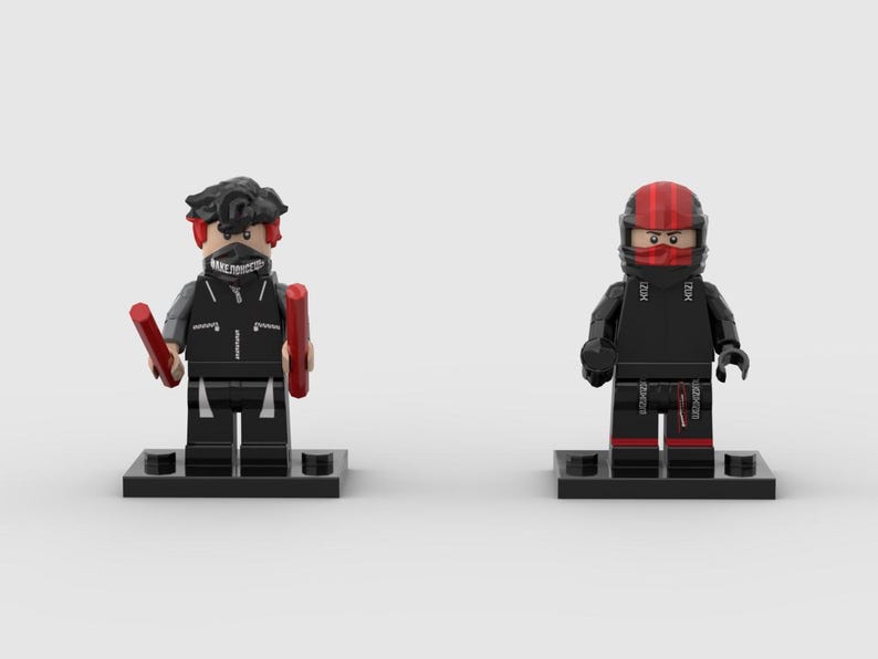 May include: Two Lego minifigures on black bases. One figure has black hair, a black vest, and holds two red batons. The other figure wears a red and black helmet and a black outfit with red accents. Both figures are on black bases.