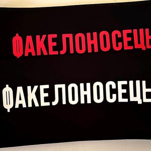 May include: Two black rectangular objects with the Russian word "ФАКЕЛОНОСЕЦ" in red and white. The red text is on the top object, and the white text is on the bottom object. The text is in a bold, sans-serif font.