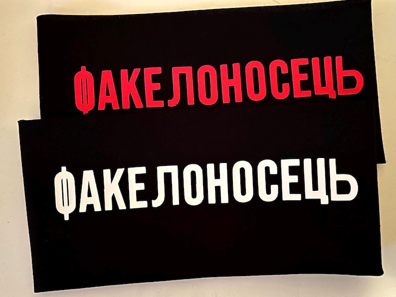May include: Two black rectangular objects with the Russian word "ФАКЕЛОНОСЕЦ" in red and white. The red text is on the top object, and the white text is on the bottom object. The text is in a bold, sans-serif font.