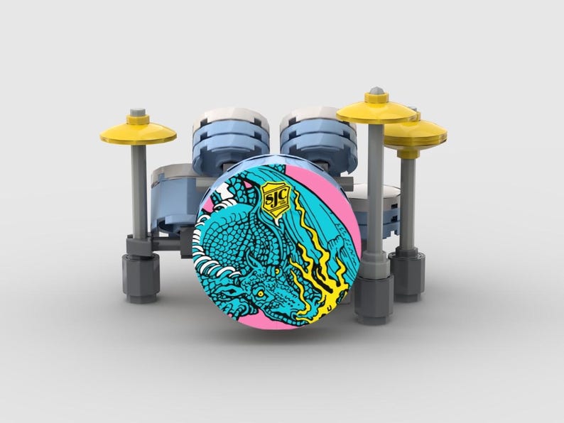 May include: A miniature drum set made of building blocks. The drum features a pink and teal graphic of a dragon. The set includes light blue drums, yellow cymbals, and gray supports.