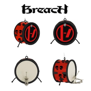 May include: Four small decorative drums are shown. Two drums have a red and black design with a stylized "-7" logo, and the other two have a white drumhead. The word "Breach" is displayed above the drums in a gothic font.
