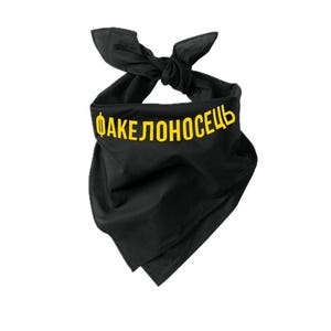 May include: Black bandana with yellow text reading "ФАКЕЛОНОСЕЦЬ". The bandana is knotted at the top, forming a triangular shape. The fabric looks to be a soft, lightweight material. The text is centered and clearly visible.