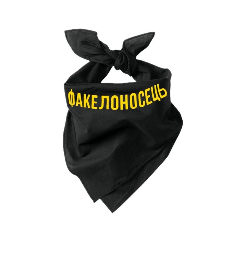May include: Black bandana with yellow text reading "ФАКЕЛОНОСЕЦЬ". The bandana is knotted at the top, forming a triangular shape. The fabric looks to be a soft, lightweight material. The text is centered and clearly visible.