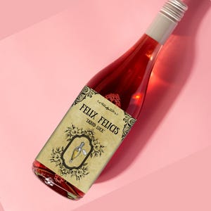 May include: A red glass bottle with a vintage-style label that reads "Felix Felicis Liquid Luck". The label features a black and white illustration of a potion bottle with a cork and a tag.