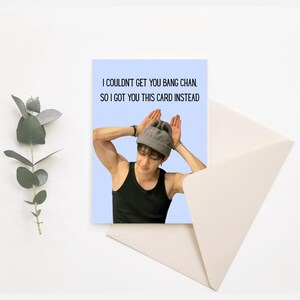 May include: A greeting card featuring a photograph of a man wearing a grey beanie and making bunny ears with his hands. The text on the card reads "I couldn't get you Bang Chan, so I got you this card instead."